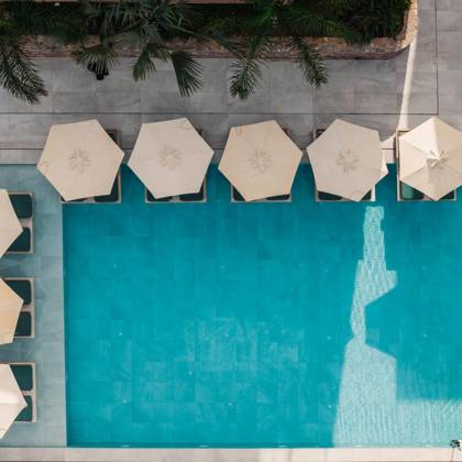 Aerial view of the main pool with sun loungers and white parasols at Paralos Venus Suites in Analipsi.