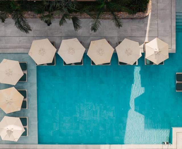 Aerial view of the main pool with sun loungers and white parasols at Paralos Venus Suites in Analipsi.