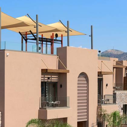 Bâtiment de l'hôtel avec balcons des suites et terrasse ombragée sur le toit, face aux montagnes