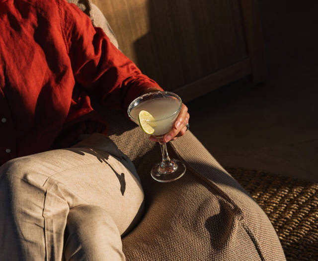 Guest in a red linen shirt holding a margarita with a salt rim and a lime slice in the warm afternoon light