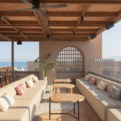 Canapés à coussins et tables basses sous une pergola en bois, avec la mer au loin